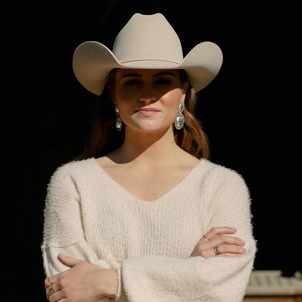 A woman wearing Concho Queen Dangle Earrings by Shop Marian and a white sweater.