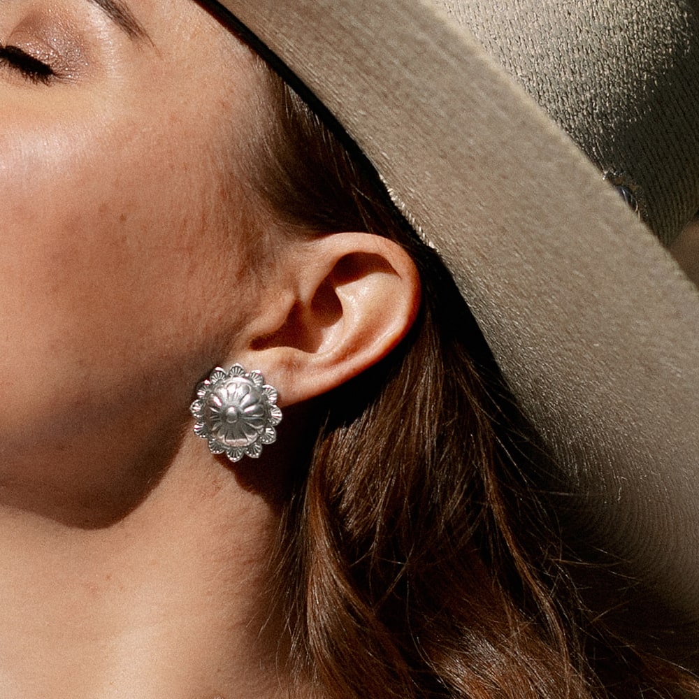 A woman wearing a cowboy hat and Concho Queen Studs earrings from Shop Marian.