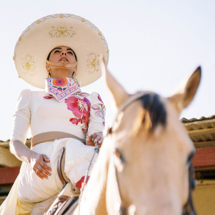 a woman wearing a Shop Marian ¡VIVA! Scarf sits on a horse.