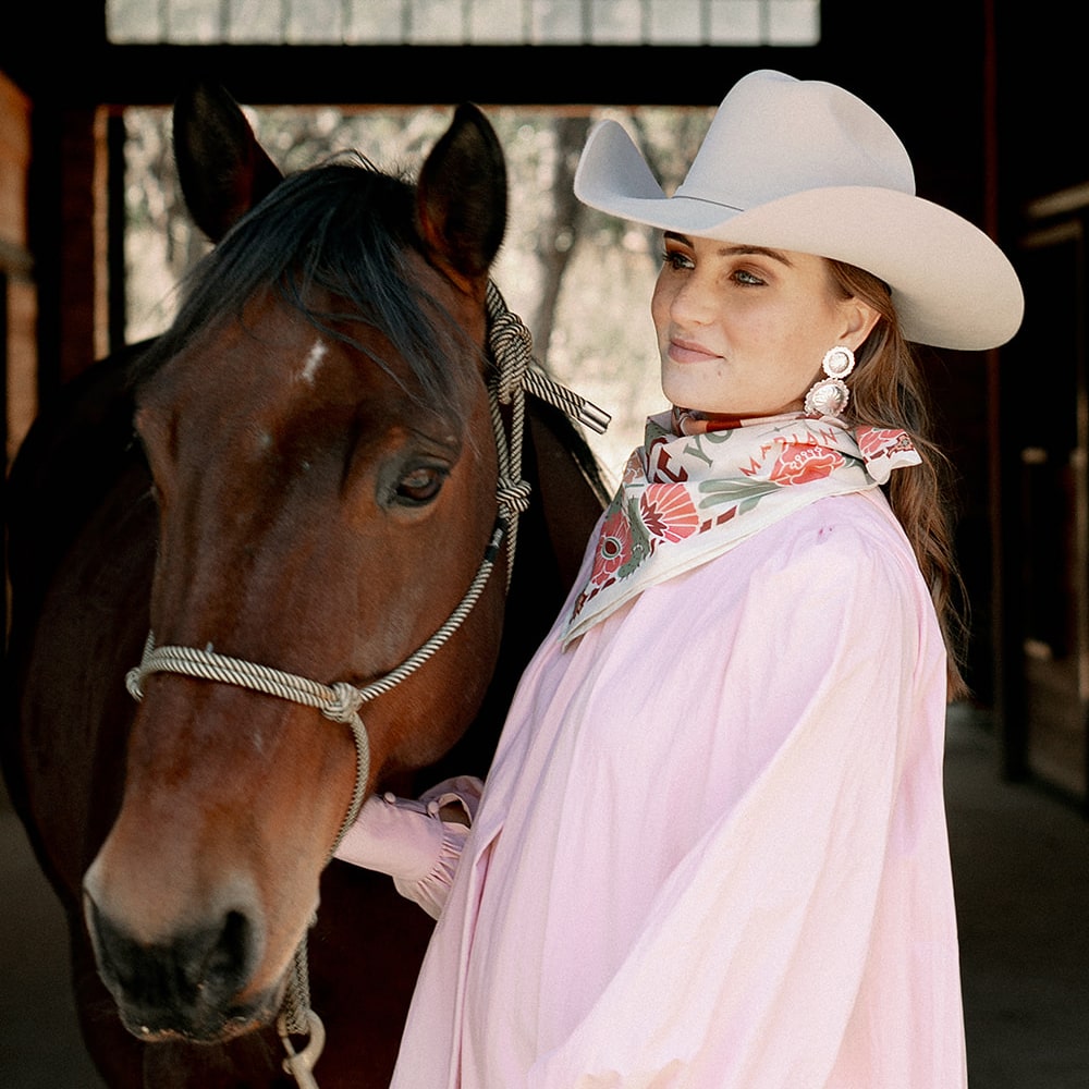 A woman in a cowboy hat standing next to a horse wearing the Catch Me Scarf from Shop Marian.