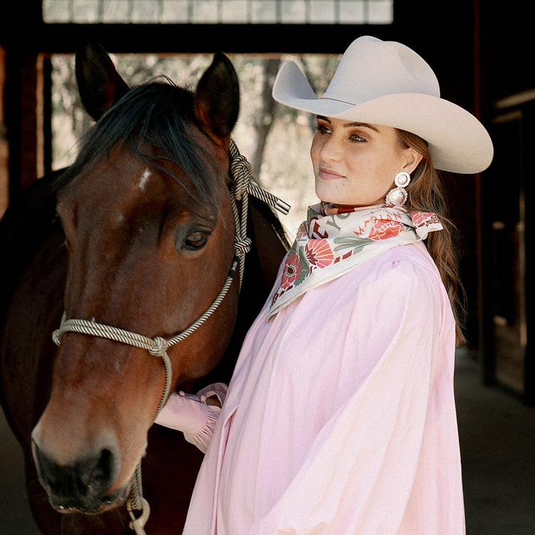 A woman in a pink dress standing next to a horse wearing the Concho Queen Dangle Earrings from Shop Marian.