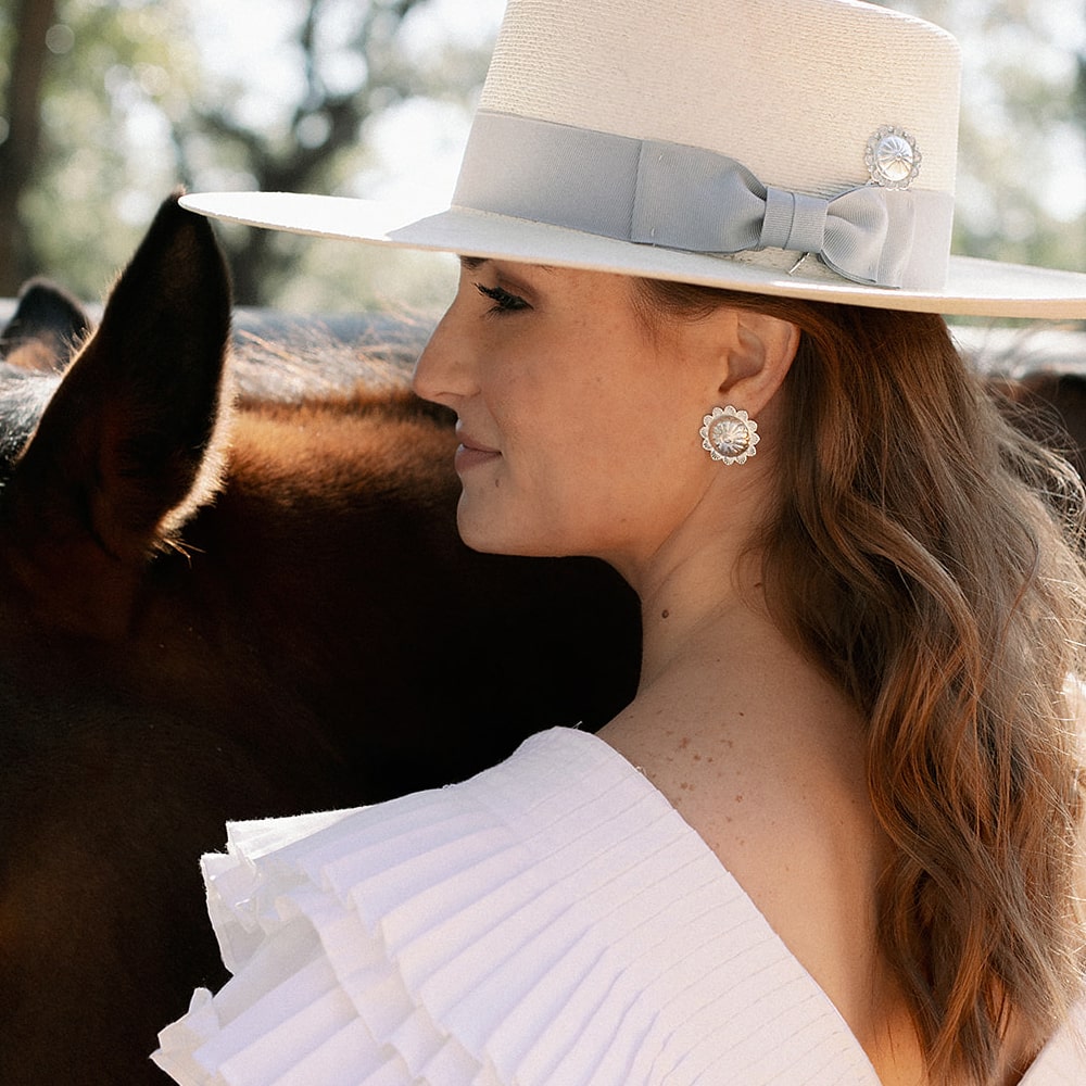 a woman wearing the Concho Queen Hat Pin from Shop Marian next to a horse.