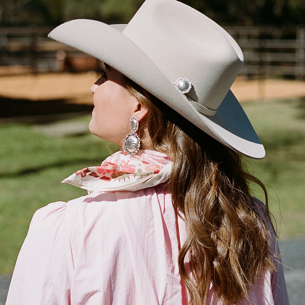 A woman wearing a Concho Queen Hat Pin by Shop Marian and pink shirt.