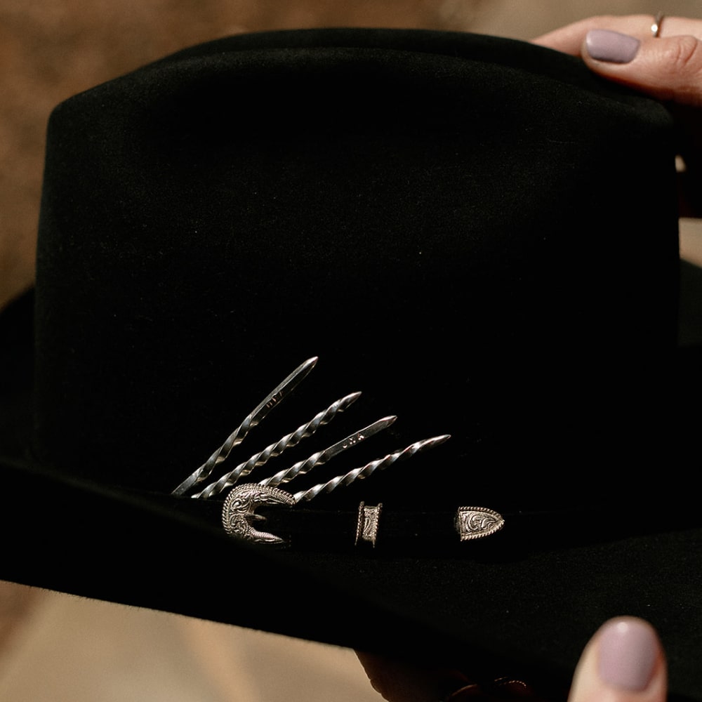 A person wearing a black Shop Marian Cowboy Toothpicks hat with a silver buckle.