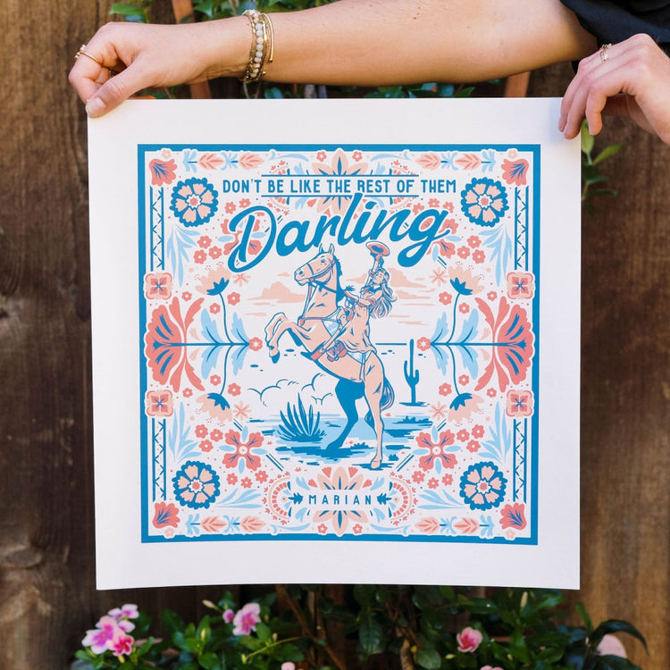 A woman is holding up a poster that says the Shop Marian Darling Print.