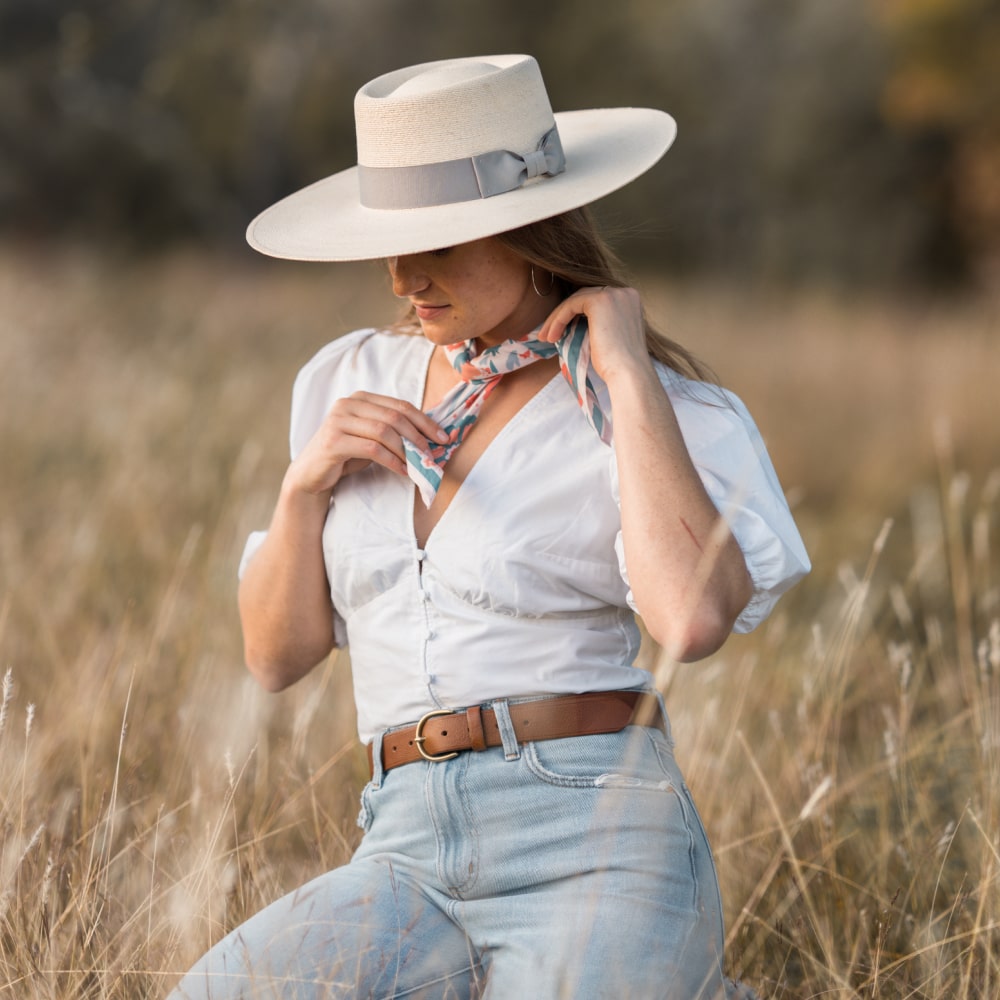 a woman wearing a Darling Scarf by Shop Marian with hat and jeans in a field.