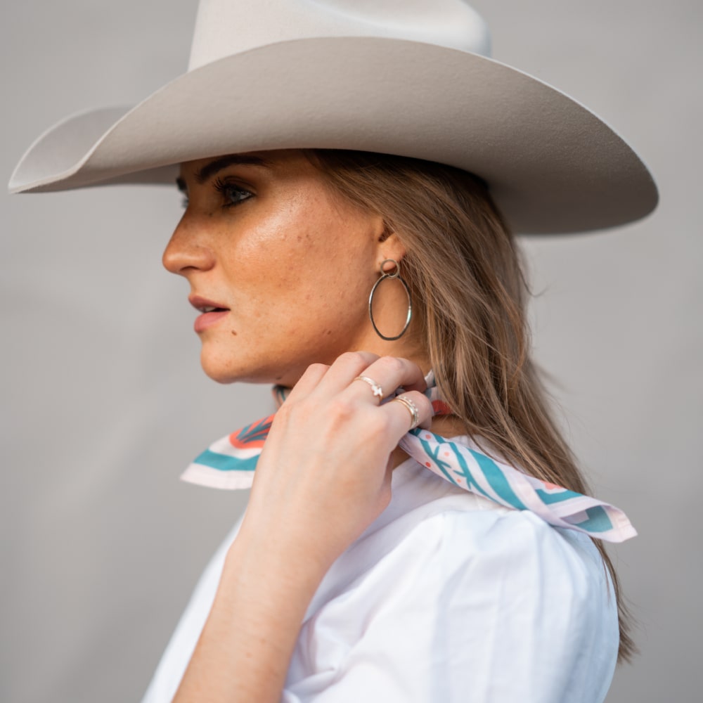 a woman wearing a Darling Scarf from Shop Marian, cowboy hat and white shirt.