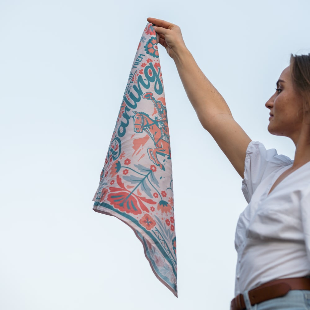 A woman is holding up the Darling Scarf from Shop Marian, which has a quote on it.