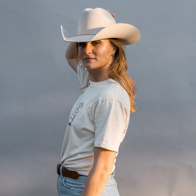 a woman wearing a Darling T-Shirt by Shop Marian, cowboy hat, and jeans.