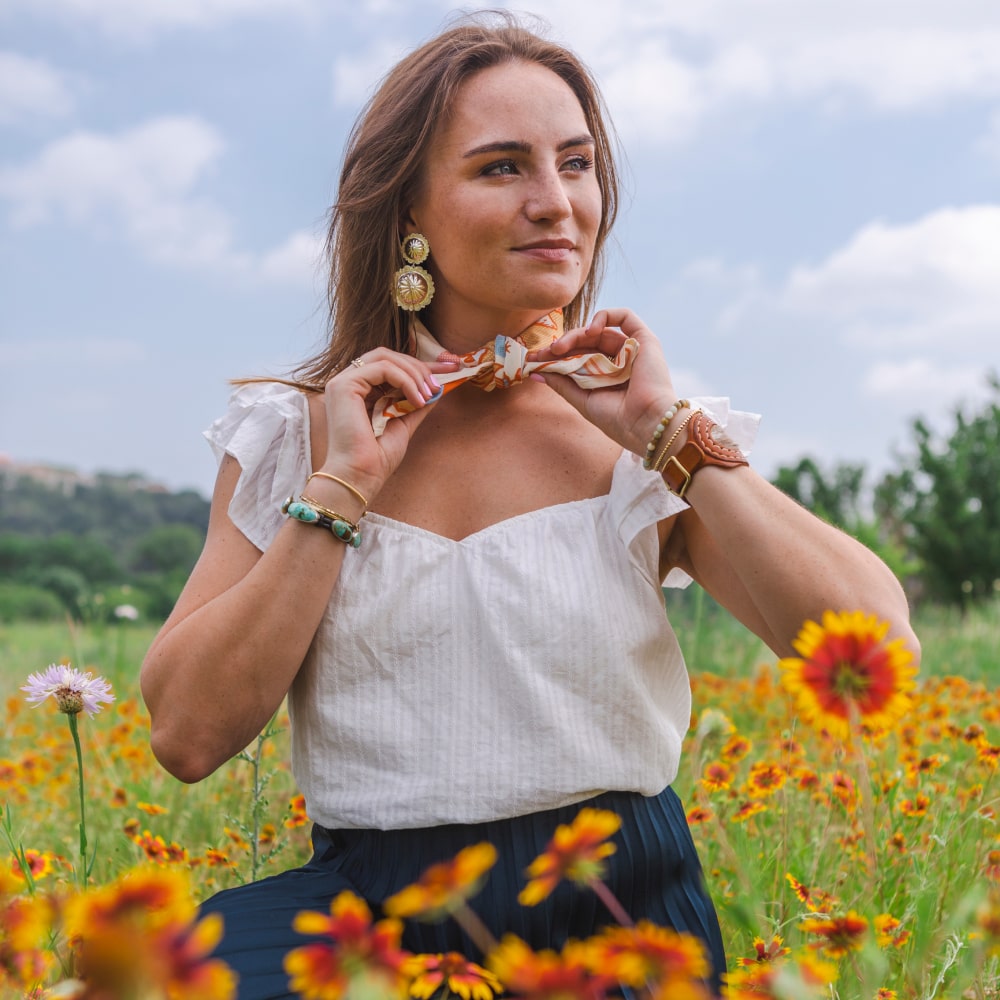 a woman sitting in a field of wildflowers holding a Grow Good Things Scarf from Shop Marian.