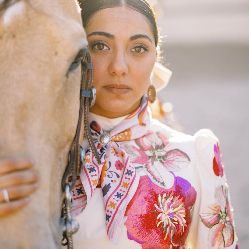 a woman in a floral dress standing next to a horse wearing the ¡VIVA! Scarf by Shop Marian.